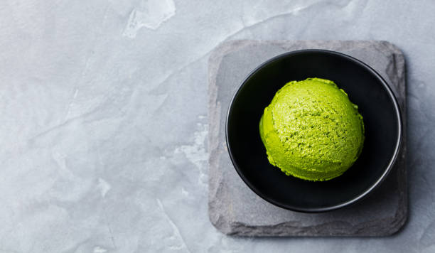 istock Green tea matcha ice cream scoop in black bowl on a grey stone background. Copy space. Top view 953936880