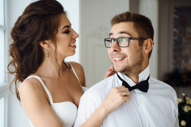 istock Grooms morning preparation with bride, handsome groom getting dressed and preparing for the wedding. Bride wearing a tie for groom 953946098