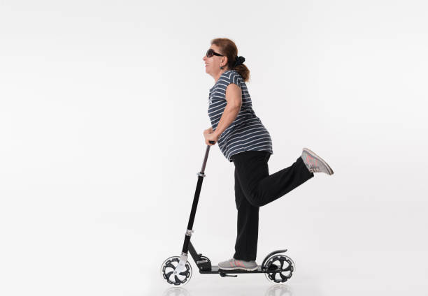 Happy mature women riding scooters over white background