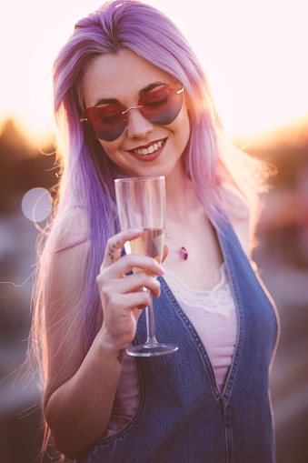 Beautiful young hipster woman with purple hair partying and drinking champagne at summer party