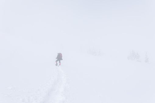 A man with a backpack standing on the snow covered hillside during trekking in the Carpathians