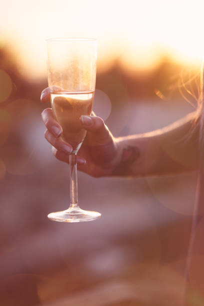 日没で、シャンパン グラスを押しの入れ墨をした若い女性の手 - flute solo ストックフォトと画像
