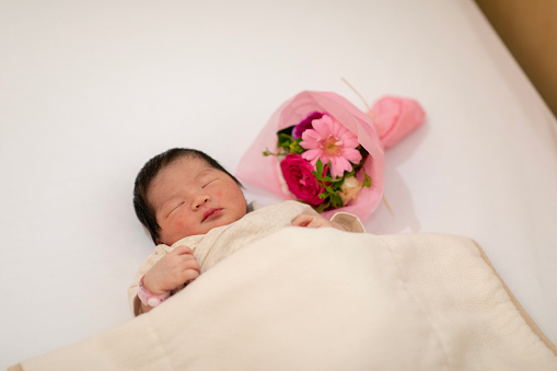 Newborn baby sleeping with bouquet on bed