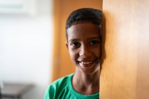 Close Up Portrait of a Shy Authentic African Boy Smiling and Laughing at the Camera with a Blurred Background. Black Male Kid Representing Future, Hope, and Acceptance. Documentary Footage