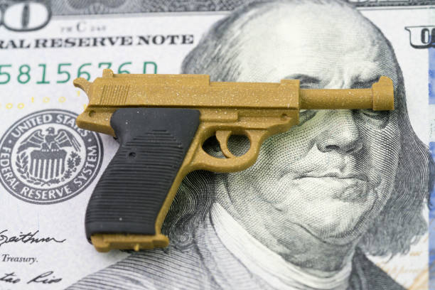 amerikanischen schusswaffe oder pistole geschäft mit viel geld konzept, gun control-richtlinie in vereinigte staaten von amerika nach vielen masse schießen, miniatur spielzeugpistolen auf franklin augen und gesicht der us-dollar-banknote - mass murder stock-fotos und bilder