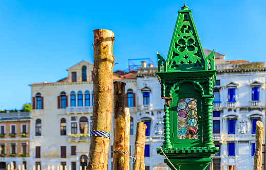 Ornate antique green lamp with wodden and glass detial at a gondola stop with traditional Venetian Gothic buildings in the background in Venice Italy
