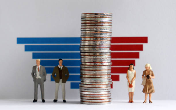 Two miniature men and two miniature women standing on both sides of a pile of coins in front of a bar graph. The concept of gender gap. stock photo