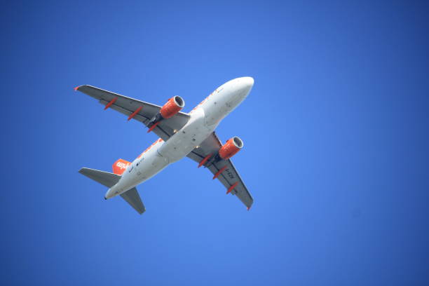 An orange easyJet plane flying against a blue sky. Clouds are visible in the sky. Airbus A321neo.