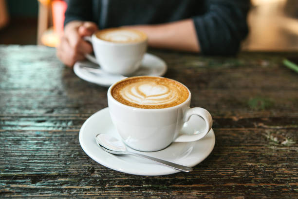 two cups of coffee on a wooden table, the girl holds in her hand one cup of coffee in the background. a photo indicates a meeting of people and a joint pastime. - cafe bar imagens e fotografias de stock