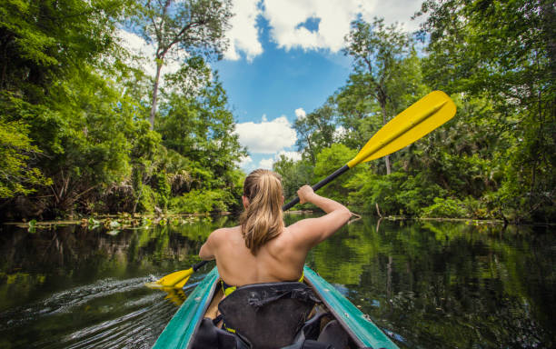 Woman Kayaking down a beautiful tropical jungle river Adventuresome Woman kayaking along a beautiful tropical jungle river. Paddling along a calm beautiful river in a scenic natural backdrop eco tourism photos stock pictures, royalty-free photos & images
