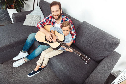 high angle view of father with son playing guitar and smiling at camera