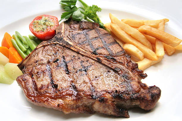 T-bone steak plated with fries and vegetables portion of t-bone steak on white plate. t bone steak stock pictures, royalty-free photos & images