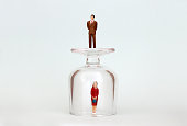 A miniature woman in a glass cup and a miniature man on top of a glass cup. The concept of the gender promotion gap.