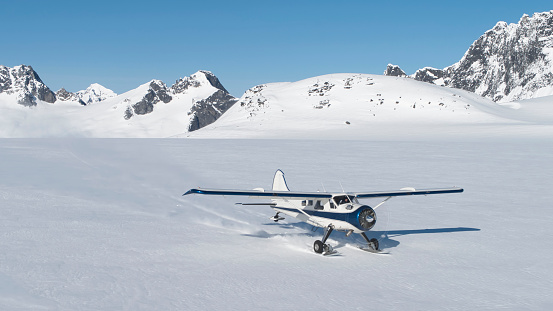 Small bush plane with skiis landing on snow in Southeast Alaskan mountains on a sunny day in spring.