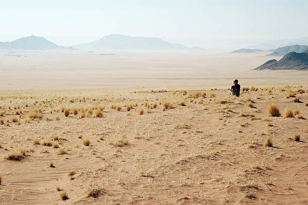 Female tourist walking in deadvlei, a white clay pan characterized by dark, dead camel thorn trees contrasted against the orange dunes