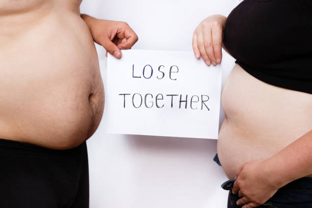 close-up portrait of man and woman obese bellies and hands holdi - dieting overweight weight scale healthcare and medicine imagens e fotografias de stock