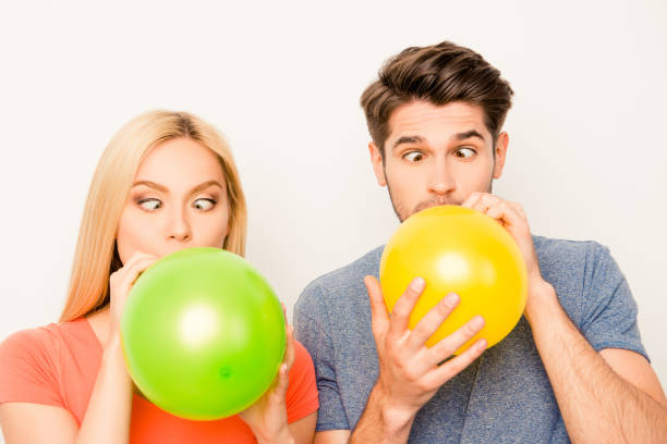 istock Two funny lovers inflating balloons for celebration and grimacing 954093322