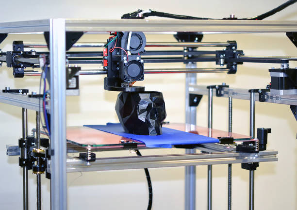 istock 3D printer printing a model in the form of black skull close-up 954098296