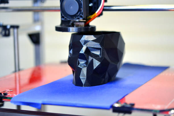 istock 3D printer printing a model in the form of black skull close-up 954101734