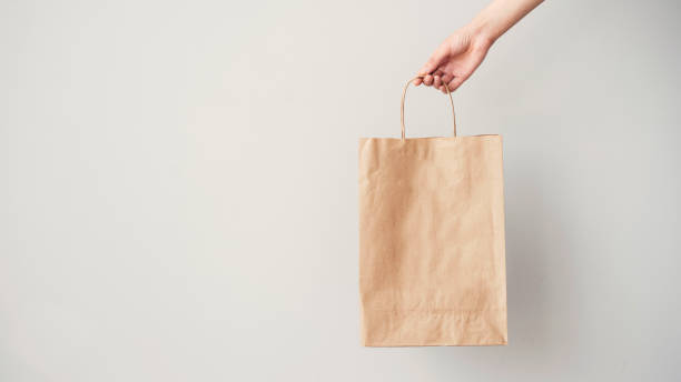 istock Female hand holding brown paper bag on grey background 954112096