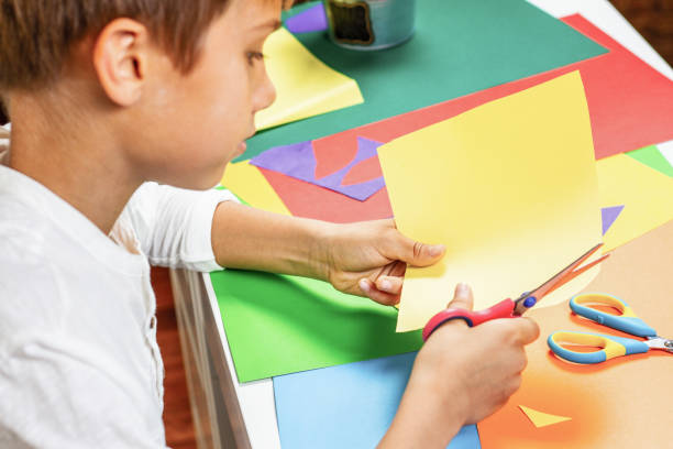 istock Child cutting colored paper with scissors at the table 954112322