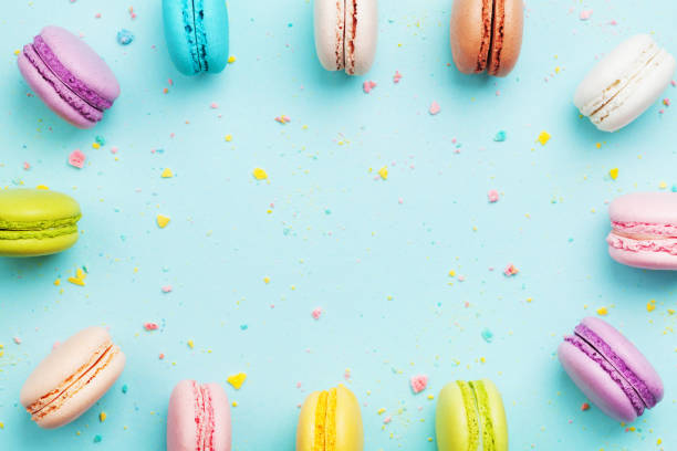 istock Colorful frame from cake macaron or macaroon on mint pastel background from above. French cookies on dessert. Flat lay. 954120632