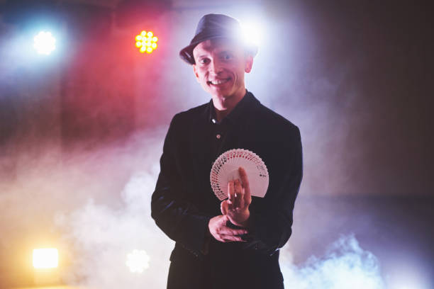 istock Magician showing trick with playing cards. Magic or dexterity, circus, gambling. Prestidigitator in dark room with fog 954125160