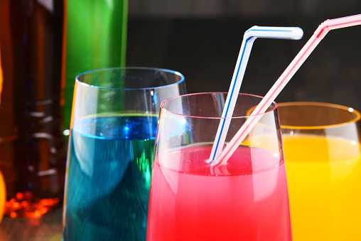 Glasses and bottles of assorted carbonated soft drinks in variety of colors