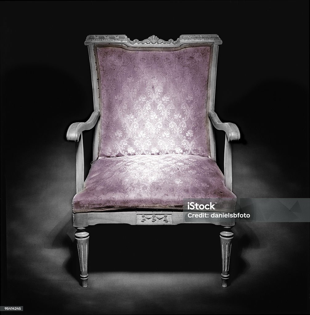 Classic armchair in a dark ambiance Old armchair in a dark ambience. Antique style. Purple color upholstery worn by time. Medium format camera shot in b&w film and colored treatment. Chair Stock Photo