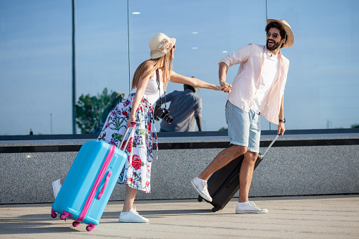 Happy young tourists holding hands and hurrying to catch a plane. Looking at each other