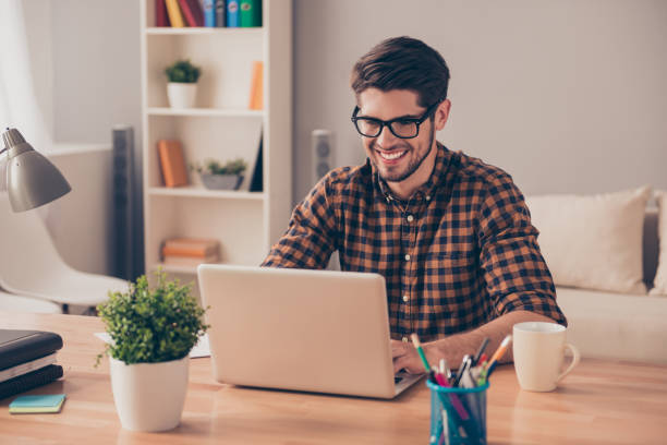 istock Handsome cheerful young man in glasses typing on laptop 954157772