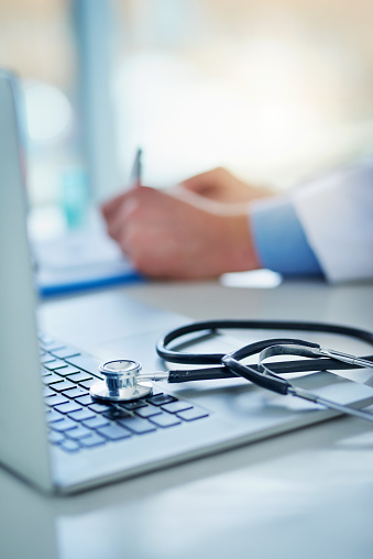 Closeup shot of a stethoscope resting on a laptop with an unrecognizable doctor working in the background