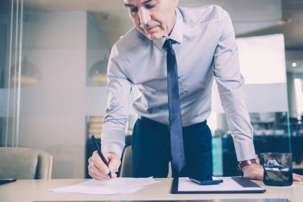 istock Senior Businessman Bending over Desk and Writing 954161914