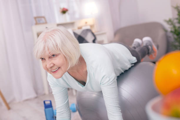 istock Cheerful elderly woman lying on balance ball and doing plank 954169112