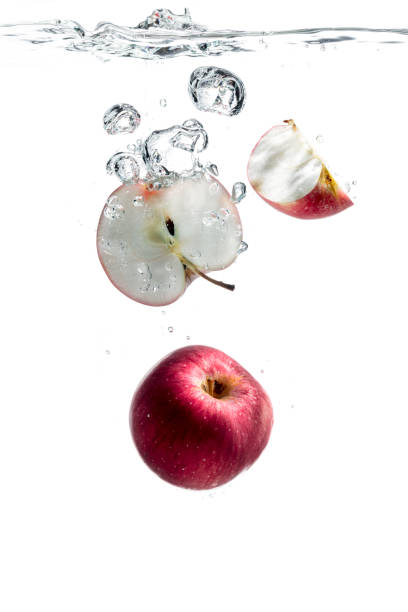 Fresh whole and sliced red apples are just thrown into water. They make bubbles while going deep into the crystal clear water on white background.