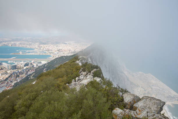 Aerial view of top of Gibraltar Rock Aerial view of top of Gibraltar Rock, in Upper Rock Natural Reserve: on the left Gibraltar town and bay, La Linea town in Spain at the far end, Mediterranean Sea on the right in fog United Kingdom, Europe. colony territory photos stock pictures, royalty-free photos & images