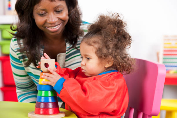 istock Smiling teacher looking at baby stacking toy rings 954191880