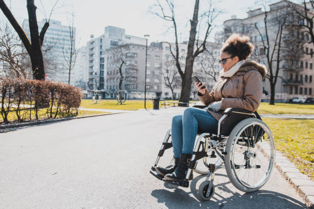 istock Disabled woman in a wheelchair using smartphone outdoors 954196944