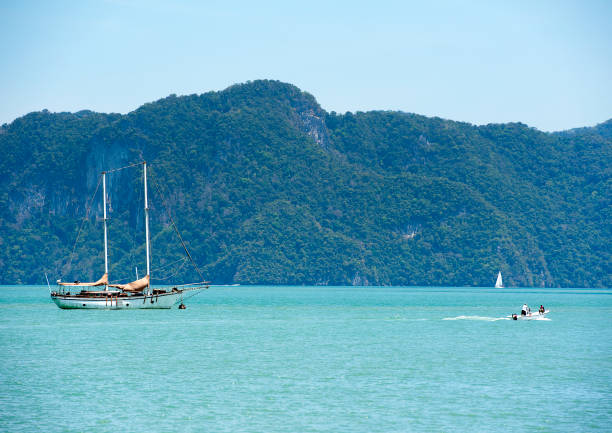 Fast Island hopper boat with outboard motor at full speed skims on the plane across the sea, past a luxury yacht or schooner, leaving a long sunlit wake, en route to one of the archipelago's numerous islands,  Langkawi, Andaman Sea, Kedah