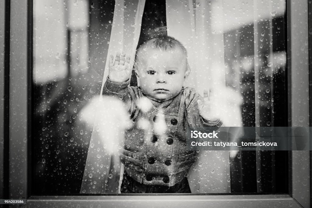 Cute toddler boy, staying at home behind the glass doors, watching outside Cute toddler boy, staying at home behind the glass doors or window, watching outside Orphanage Stock Photo