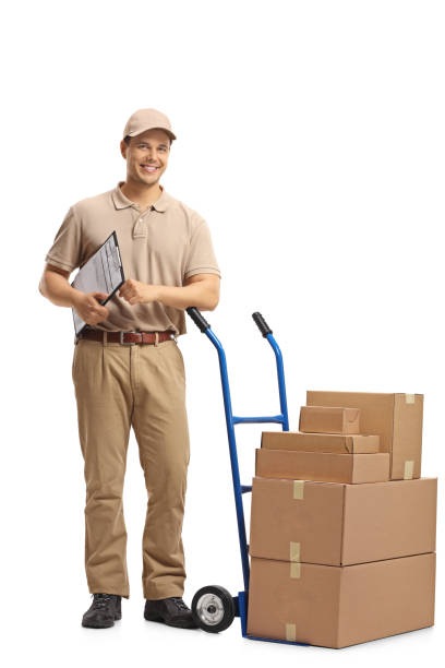 istock Delivery man with a clipboard leaning on a hand truck with a stack of boxes 954214370