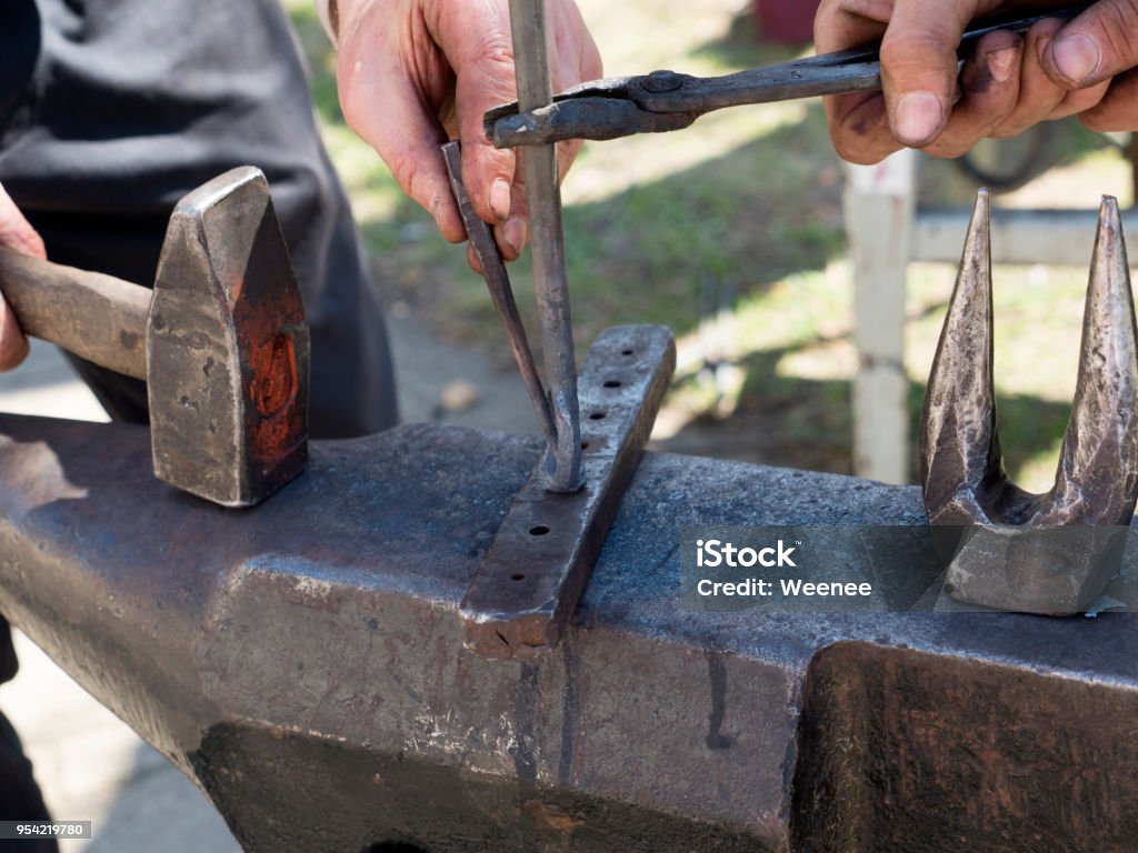 Blacksmith forge with hammer iron on anvil Blacksmith forge with hammer iron on anvil. Detail of working hands. Daily sunshine Metalwork Stock Photo