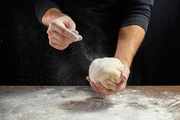 close-up de chef masculino mãos, sove a massa, cozinhe a massa em um fundo escuro. - bread kneading making human hand - fotografias e filmes do acervo