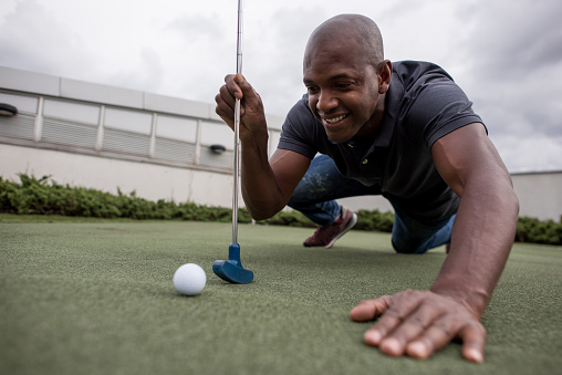 Black handsome man having fun playing mini golf smiling very happy