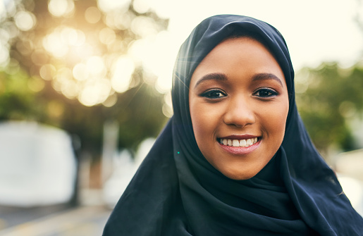 Portrait of a cheerful young woman standing alone and smiling to the camera  outside during the day