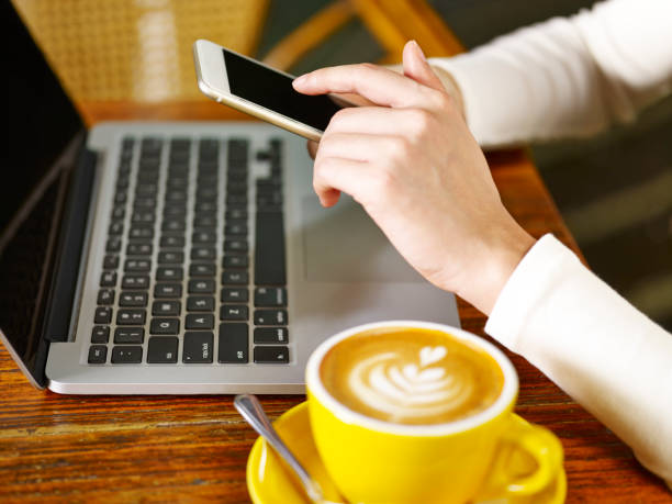 istock woman using cell phone and laptop in coffee shop 954246184