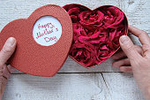 Womans hands holding heart box gift with fresh roses for Mother's day. Gratefulness present concept