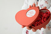 Front view of womans hands holding heart box gift with fresh roses for Mother's day. Gratefulness present concept