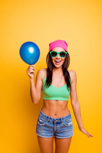 chica hipster emocionado alegre sombrero rosa con globo en la pared amarilla - balloon blowing inflating child fotografías e imágenes de stock