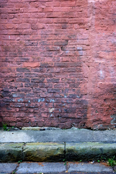 istock An old brick wall with faded paint with road and rain water gutter in front. 954252138